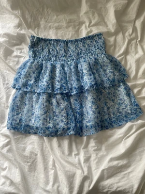 Blommig blå volangkjol  - Kort blå blommig volang kjol från Vero Moda. Går även andvända som topp