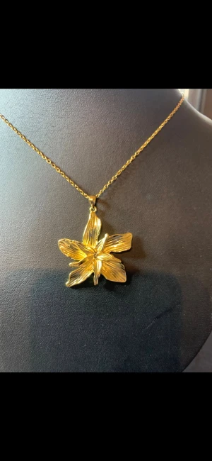 Guldigt halsband med blomma - Snyggt halsband i guldfärg med ett stort blomformat hänge. Kedjan är tunn och smidig medan hänget har en detaljerad design med fem blad som ger ett elegant intryck. Perfekt accessoar för dig som gillar blommiga smycken och vill sticka ut.