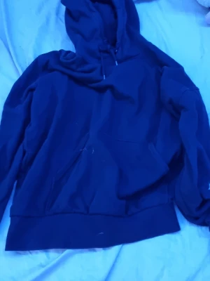 Svart hoodie från Weekday - En klassisk svart hoodie från Weekday med huva och känguruficka framtill. Tillverkad i mjukt bomullsmaterial och har ribbade muddar vid ärmslut och nederkant. Perfekt för en chill och avslappnad stil.