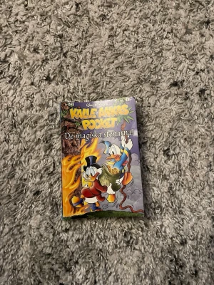 Kalle Ankas Pocket: De magiska stenarna - Rolig pocketbok från Disney-serien Kalle Ankas Pocket, nummer 243, med titeln 'De magiska stenarna'. Färgglad framsida med Kalle Anka och Farbror Joakim på äventyr. Mjuk pärm i klassisk pocketformat, perfekt för dig som gillar serier och äventyr.