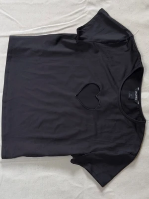 Svart t-shirt med hjärtdetalj Monki - Svart t-shirt från Monki i mjuk bomull, kortare i midjan, använd ett fåtal gånger. 