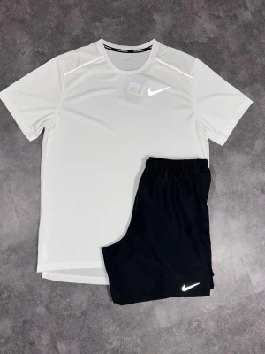 Nike träningsset t-shirt och shorts - Snyggt träningsset från Nike med en vit t-shirt och svarta shorts. T-shirten har rund hals och korta ärmar, båda plaggen har Nike-logga framtill. Perfekt för gymmet eller löpning. Materialet är lätt och andas bra.