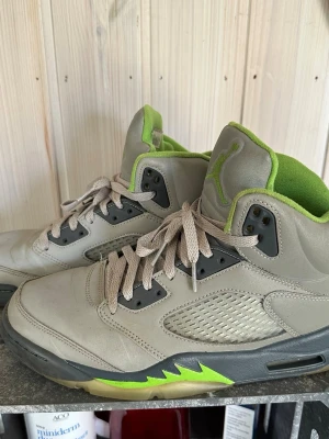 Air Jordan 5 Retro grå/lime - Snygga Air Jordan 5 Retro sneakers i grått läder med limegröna detaljer och svart sula. Skorna har meshpaneler på sidorna, klassisk Jumpman-logga på plösen och limegrönt foder. Perfekta för dig som gillar streetwear och vill sticka ut.