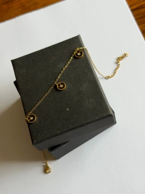 Guldigt fotlänk med cirkelhängen - Snyggt och tunt fotlänk  i guldfärgad metall med tre små cirkelformade hängen. Kedjan är finlänkad och har ett klassiskt lås. Perfekt för dig som gillar minimalistiska smycken med en modern touch.