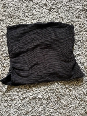 Svart ribbad tubtopp - En svart ribbad tubtopp som är perfekt för att skapa en stilren och enkel look. Toppen är axelbandslös och har en tight passform. Toppen är i storlek XS från H&M