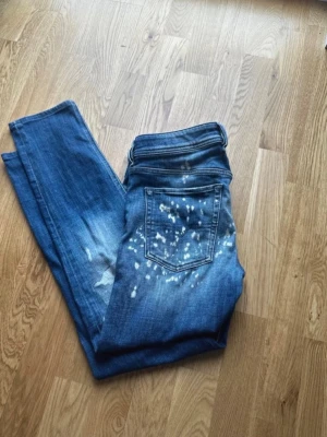 Blå jeans från Diesel - Snygga blå skinny jeans från Diesel, modell Sleenker-X. Jeansen har coola blekta detaljer och stänk på baksidan . Tillverkade i stretchigt denim för en bekväm passform. Perfekta för dig som gillar en trendig och avslappnad stil. Storlek 32, är lite slitna vid knäet men passar in på slitningarna