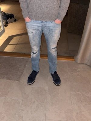 Jack and jones jeans - Säljer ett par ljusblå jeans med skinny fit och slitna detaljer samt hål på båda knäna. Jeansen har klassisk femficksdesign och är tillverkade i denim med en snygg tvättad look. Perfekta för en avslappnad och trendig stil.