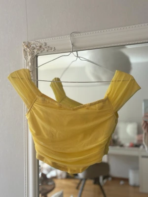 Gul croppad topp med dragkedja - Trendig gul croppad korset liknande topp med breda axelband och snygga rynkade detaljer. Toppen har en dragkedja i ryggen. Perfekt för dig som vill sticka ut med färg och stil. 