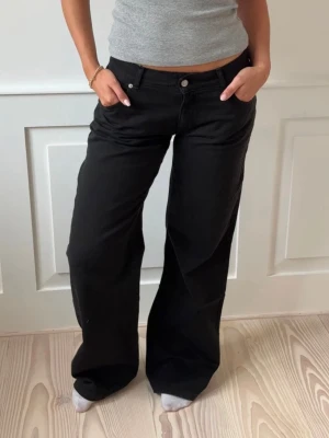 Svarta vida jeans med låg midja - Säljer ett par svarta jeans med låg midja och breda, raka ben. Jeansen har klassisk femficksmodell och stängs med knapp och dragkedja. Perfekta för en avslappnad och trendig look. Helt oanvänd mer prislappen kvar!! Nypris 802kr