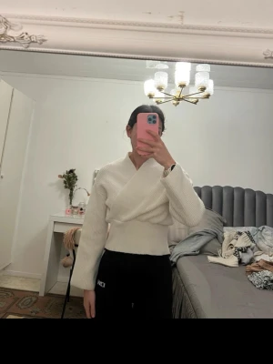 Vit omlottstickad tröja - Säljer en vit stickad tröja med omlott-design och breda ribbade muddar. Tröjan har lång ärm och är något croppad i modellen. Perfekt för dig som gillar en enkel men trendig look.