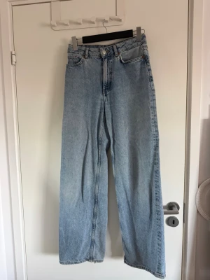 Ljusblå raka jeans - Säljer ett par ljusblå jeans med rak passform och hög midja. Jeansen har klassiska fem fickor, knappgylf och en liten slitning på ena bakfickan. Tillverkade i denim av bomull för en tidlös look.