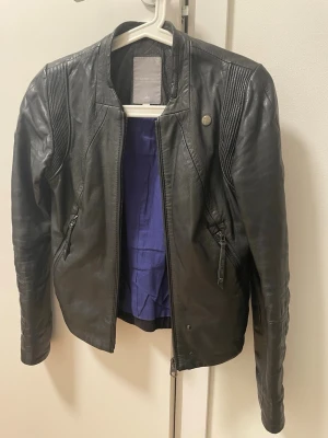 Svart skinnjacka från G-Star RAW XS - Snygg svart skinnjacka från G-Star RAW i storlek XS. Jackan har dragkedja framtill, två fickor med dragkedja och coola detaljer på axlar och ärmar. Fodret är lila och jackan har en modern, figurnära passform.