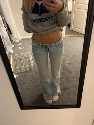 Ljusblå bootcut jeans - Säljer ett par ljusblå bootcut jeans med låg midja och klassisk femficksmodell. Jeansen har en snygg tvätt och är tillverkade i denim med lite stretch för skön passform. Perfekta till en avslappnad och trendig look.