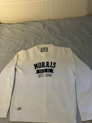 Vit tröja från Morris - Snygg vit tröja från Morris med svart texttryck 'MORRIS PHYS. ED. EST. 1968' på bröstet. Tröjan har rund halsringning, ribbade muddar. Perfekt för en avslappnad och sportig stil.