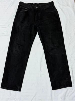 Svarta raka jeans 36x30 - Säljer ett par svarta jeans med rak passform. Klassisk femficksmodell och knappgylf. Jeansen har en enkel och stilren look som passar till det mesta. Perfekta för dig som gillar en avslappnad men ändå snygg stil.