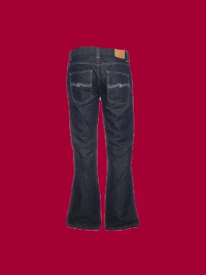 Nudie Jeans - Säljer ett par mörkblå jeans från Nudie Jeans 2001 med klassisk femficksmodell och kontrastsömmar. Jeansen har raka ben, snygga slitningar framtill och broderade bakfickor. Tillverkade i kraftigt denimtyg som ger en cool och tidlös look.