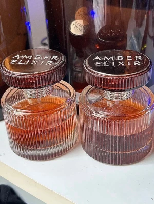 Amber Elixir parfume 50ml  - Amber Elixir parfym i rund glasflaska med räfflad yta och bruntonad färg. Locket är metallicasilver med texten 'Amber Elixir' ingraverad. Flaskan har en elegant och lyxig design som sticker ut på hyllan. Nypris 1st 600kr, säljer båda för 600kr (flaskorna har enbart damm på sig) 