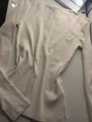 Vit ribbad långärmad topp från H&M - Säljer en stilren vit långärmad topp från H&M, tillverkad av 20% återvunnen bomull. Toppen har en ribbad struktur och en slim passform som framhäver siluetten. Perfekt att matcha med jeans eller kjol för en clean look.