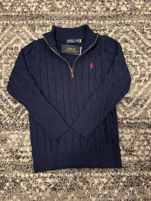 Marinblå kabelstickad tröja Polo Ralph Lauren - Kabelstickad marinblå tröja från Polo Ralph Lauren med halv dragkedja. Klassisk röd logga på bröstet. Tröjan är i storlek M men passar även i storlek S!! Hör av er vid eventuella frågor eller funderingar!!