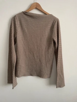 Beige långärmad topp med struktur - Säljer en beige långärmad topp med vågig struktur i materialet. Tröjan har en enkel, rak passform och är tillverkad i ett mjukt tyg som ger en skön känsla. Perfekt för dig som gillar stilrena plagg med det lilla extra i texturen.