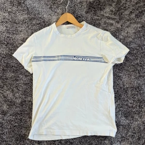 Moncler t-shirt - Säljer en vit t-shirt från Moncler med blått tryck och ränder över bröstet. Passar perfekt nu till våren! Hör av er med frågor 