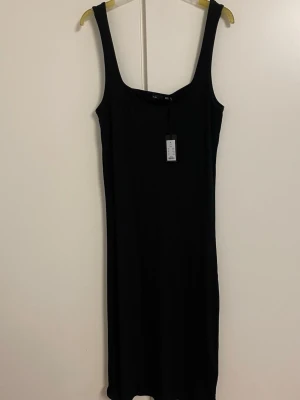 Svart ribbad långklänning H&M - Svart ribbad långklänning från H&M med breda axelband och fyrkantig ringning. Klänningen har en kroppsnära passform och är tillverkad i ett stretchigt material som ger en snygg siluett. Perfekt för dig som gillar minimalistisk stil.