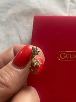 Guldörhängen 18K Blommiga örhängen i guld från Guldfynd - Snygga örhängen i guld från Guldfynd med blommig design och glittrande stenar i mitten. Perfekta för dig som gillar klassiska men ändå unika smycken. Stiftmodell som sitter bekvämt på örat.Stämplade Äkta guld!