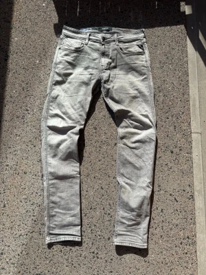 Grå slim fit jeans från Replay - Snygga grå slim fit jeans från Replay, modell Anbass. Jeansen har klassisk femficksdesign, dragkedjegylf och är tillverkade i ett mjukt denimtyg med lätt tvättad look. Perfekta för dig som gillar en modern och avslappnad stil.storlek 34/32