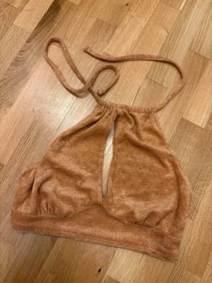 Brun frotté halterneck topp ASOS - Säljer en brun halterneck topp från ASOS DESIGN i mjuk frotté. Toppen har knyt i nacken och en öppen detalj framtill som ger en trendig look. Perfekt för dig som vill sticka ut med en unik och bekväm topp.