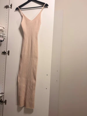 Beige ribbad långklänning - Trendig beige långklänning med smala axelband och v-ringning. Klänningen är ribbad och har en tight passform men jätte stretchg som framhäver figuren. Perfekt för dig som gillar minimalistisk och stilren design.