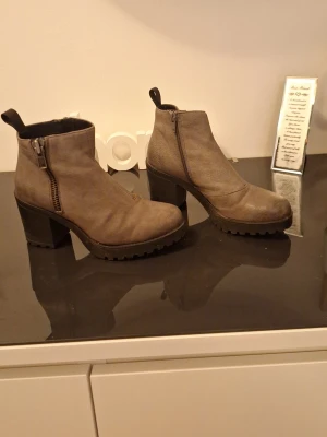 Grå/bruna stövletter med klack från Vagabond - Säljer ett par grå/bruna stövletter med grov sula och klack. Skorna har dragkedja på sidan och har en dragkedja för utseendets skull. Perfekt för dig som gillar en cool och robust stil.