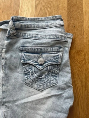 True Religion ljusblå low rise flare jeans - Nytt sick orginal pris 1500 Säljer ett par ljusblå True Religion jeans, modell Joey Low Rise Flare. Jeansen har en snygg ficka med lock och dekorativ söm bak samt silverfärgad knapp. Klassisk tvättad denim med låg midja och utsvängda ben. Perfekta för en trendig och avslappnad stil.
