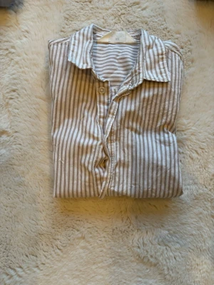 Randig kortärmad skjorta i bomull - Snygg kortärmad skjorta med beige och vita ränder. Skjortan har klassisk krage, knappar framtill och är gjord i mjuk bomull som känns skön mot huden. Perfekt för en avslappnad och stilren look.