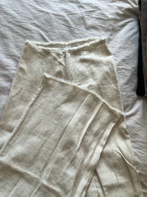 Beige omlottkjol i linne - Säljer ett par beigea kostymbyxor i linne med omlottdesign och råa kanter i midjan. 
