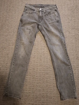 Gråa Levi's jeans - Säljer ett par gråa levis jeans med passform 514 och klassisk femficksdesign, Storlek 29W 32L. Perfekta för dig som gillar en tidlös och enkel stil. Har skada på fram benet men är lagade. Skrive vid frågor.
