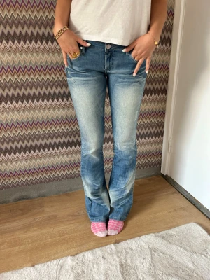 Blå bootcut jeans med låg midja - Säljer ett par blå bootcut jeans med snygga slitningar och ljusare partier framtill. Jeansen har klassisk femficksmodell, normal midja och dragkedja med knapp. Perfekta för en avslappnad och trendig look.
