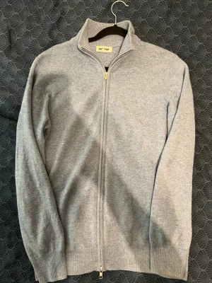 Ljusblå ziptröja från Soft Goat - Snygg ljusblå stickad ziptröja från Soft Goat med hög krage och hel dragkedja framtill. Tillverkad i mjukt material, troligen kashmir eller ullblandning. Perfekt för lager på lager och enkel att matcha med olika outfits. Litet hål i armhålan, går att lämna in hos skräddaren till lagning för en billig slant. 