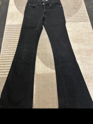 Svarta utsvängda jeans - Säljer ett par svarta jeans med hög midja och riktigt utsvängda ben. Klassisk femficksmodell med knapp och dragkedja fram. Jeansen har en cool retrovibe och passar perfekt till sneakers eller boots. Materialet är mjukt denim som sitter snyggt. De är från Gina tricot . Storlek:36