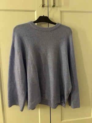 Ljusblå oversized stickad tröja - Mysig oversized stickad tröja i ljuslila med rund halsringning och långa ärmar. Tröjan har en avslappnad passform och ribbade muddar vid ärmslut och nederkant. Perfekt för lager på lager och chill dagar.