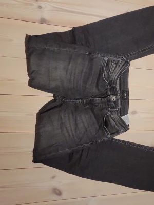 Svarta croppade jeans från Only - Säljer ett par svarta/ mörk gråa jeans från Only med råa, fransiga benslut. Jeansen har klassisk femficksmodell, knappgylf och en tvättad look med lätt slitning på låren. Perfekta för en avslappnad och trendig stil.
