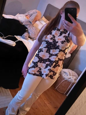 Blommig ärmlös topp från Bik Bok - Säljer en snygg ärmlös topp från Bik Bok med blommigt mönster i svart, vitt och beige. Toppen har rund halsringning och rak passform, perfekt till jeans eller kjol. Materialet känns lätt och skönt mot huden. Sval och super fin. Har öppning på båda sidor av magen och det sitter super på, visar ej för mycket. Normal i storlek och bra passform. 