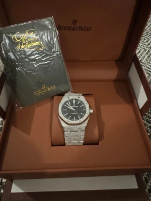 AP Royal Oak diamantklocka - Lyxig AP Royal Oak klocka med glittrande silverfärgat armband och boett täckt av diamanter. Svart urtavla med vita index och automatisk rörelse. Kommer i originalbox.