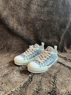 Dior B23 låga sneakers monogram - Säljer ett par Dior B23 låga sneakers med genomskinligt material och vitt monogrammönster. Skorna har vita snören, vit sula och tydliga Dior-loggor på sidan. Perfekta för dig som vill sticka ut med en lyxig och modern look.