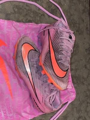 Ordinarie pris 3100 Nike Mercurial rosa fotbollsskor - Säljer ett par Nike Mercurial Elites fotbollsskor i rosa med orange och svart swoosh. Skorna har hög krage för extra stöd och är tillverkade i ett lätt, syntetiskt material. Levereras med matchande rosa Nike-påse. Perfekta för dig som vill sticka ut på planen.