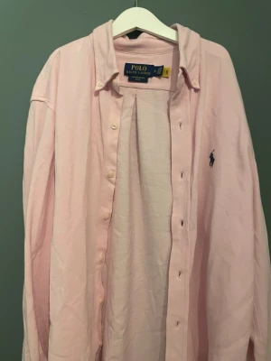 Ljusrosa skjorta från Polo Ralph Lauren - Säljer en ljusrosa skjorta från Polo Ralph Lauren i featherweight mesh. Skjortan har klassisk krage, knappar framtill och den ikoniska broderade loggan på bröstet. Perfekt för dig som gillar stilrena och tidlösa plagg.