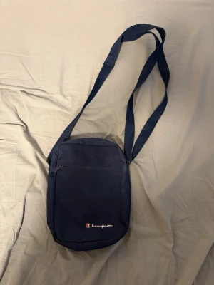 Mörkblå axelväska från Champion - Hej, säljer en mörkblå axelväska från Champion. Den är i onesize, jättebra skick inga skador eller sådant.. 