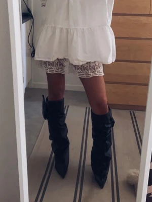 Svarta slouchy boots i skinn - Säljer ett par svarta slouchy stövletter med spetsig tå och hög klack. Tillverkade i mjukt skinn som ger en cool, rynkad look. Perfekta för dig som vill ha statement boots med edgy vibe. Passar till både klänning och jeans.