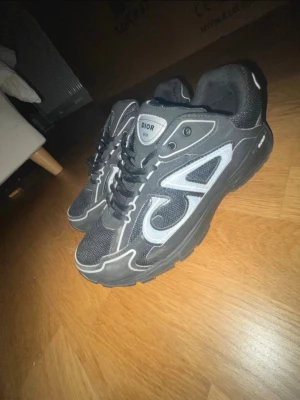 Svarta Dior sneakers pris kan disscuterad - Säljer ett par svarta Dior sneakers med vita och grå detaljer. Skorna har en chunky sula, meshpaneler och reflekterande inslag längs sidorna. Klassisk snörning och logga på plösen. Perfekta för dig som gillar streetwear och exklusiv stil.