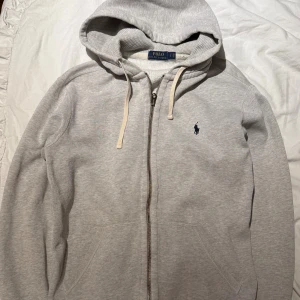 Grå hoodie från Polo Ralph Lauren - Säljer en stilren grå hoodie från Polo Ralph Lauren. Tröjan har en liten skavank som syns på sista bilden, därav priset. Nypris är 1999kr. Hör av er vid minsta lilla 🙃