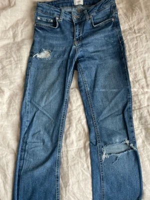Blå slitna jeans från Grunt - Ett par blå jeans från Grunt med bootcut och slitningar på både lår och knä. Klassisk femficksmodell med dragkedja och knapp. Jeansen har en avslappnad vibe och är tillverkade i denim med snygg tvätt. Skriv om ni har andra frågor!🥰